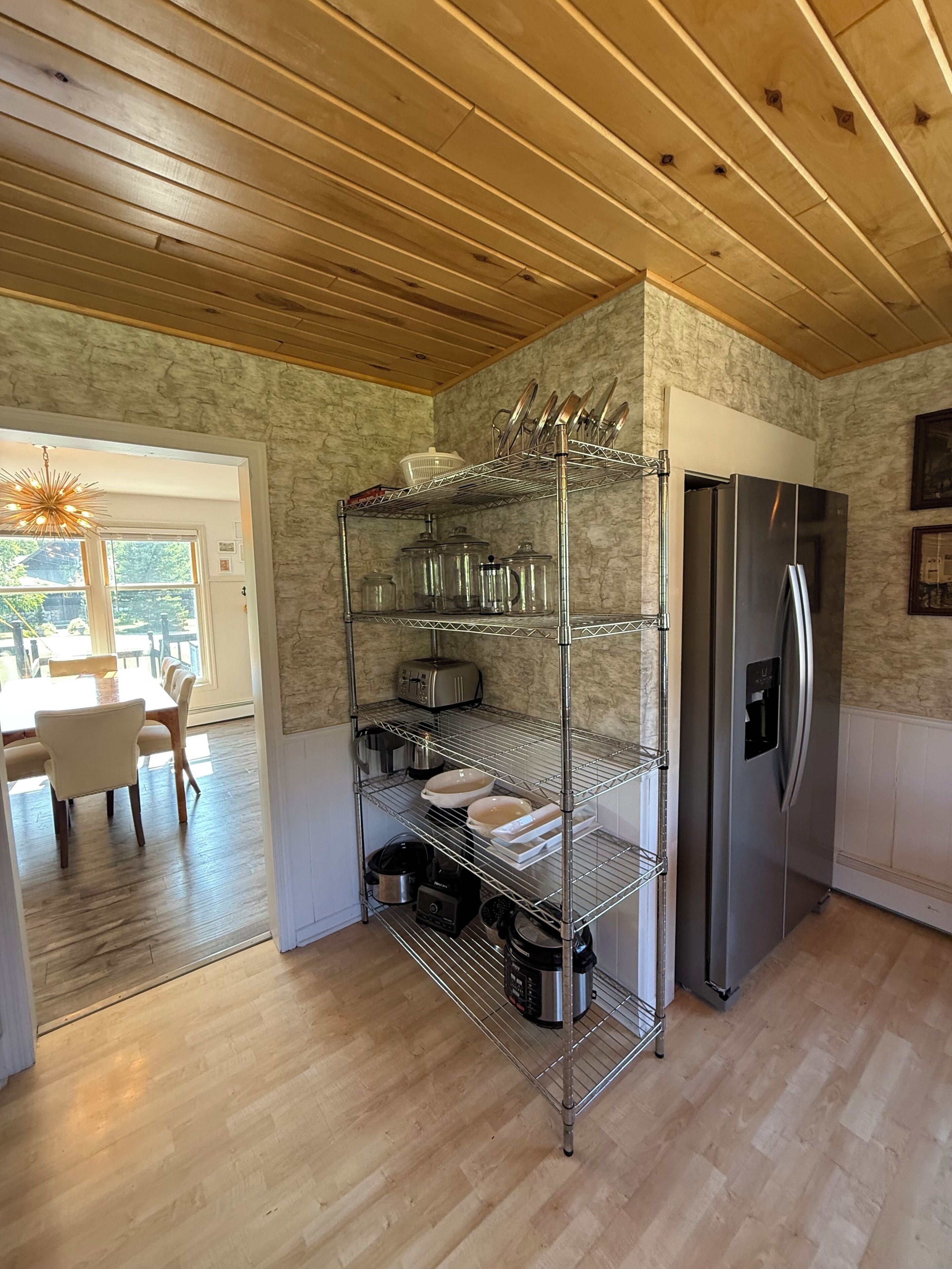 Una cocina con un refrigerador de acero inoxidable, una estantería metálica y un comedor con mesa y sillas.