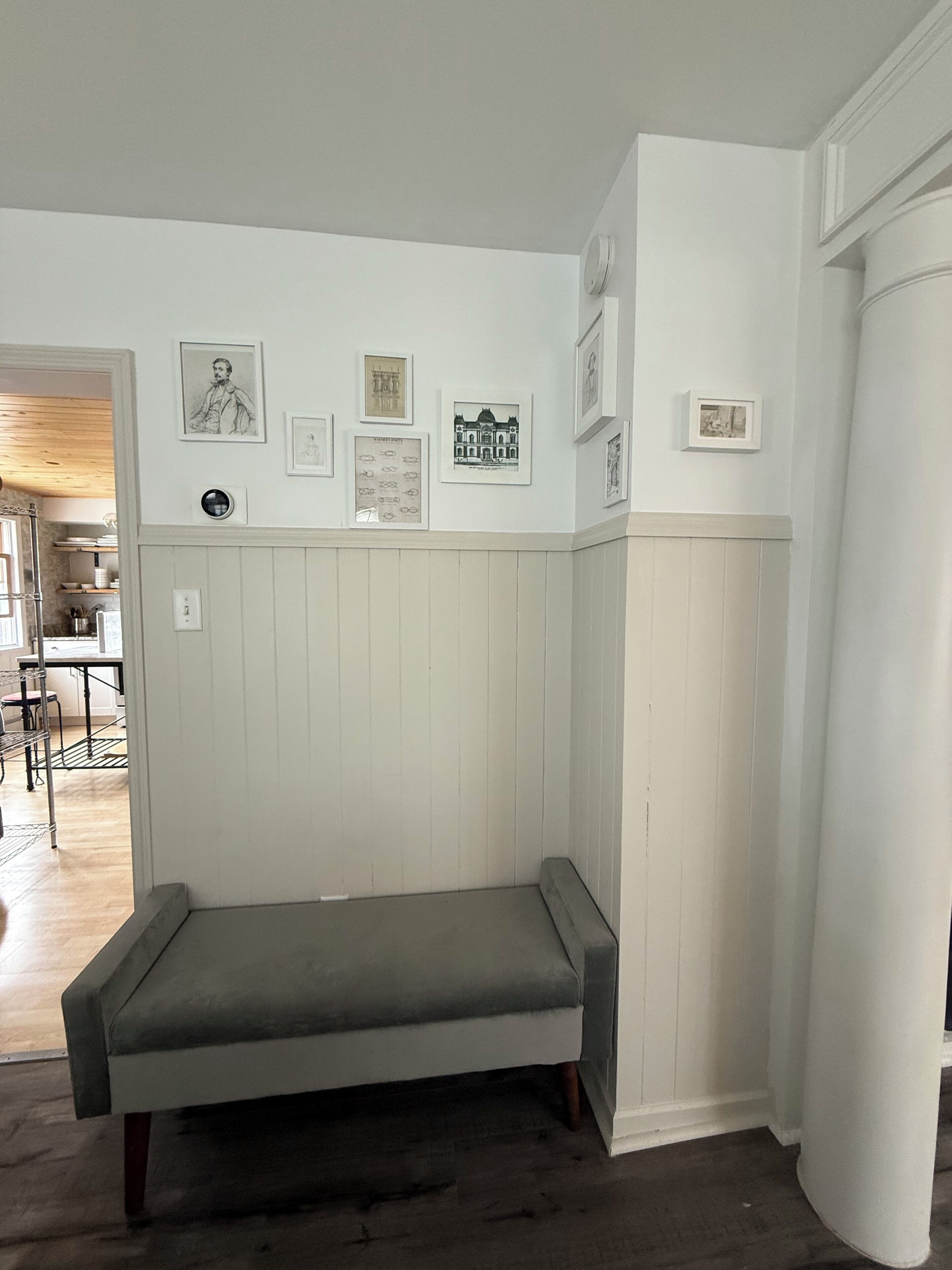 Ein Zimmer mit einer Bank, weißen Wandverkleidungen und gerahmten Bildern.