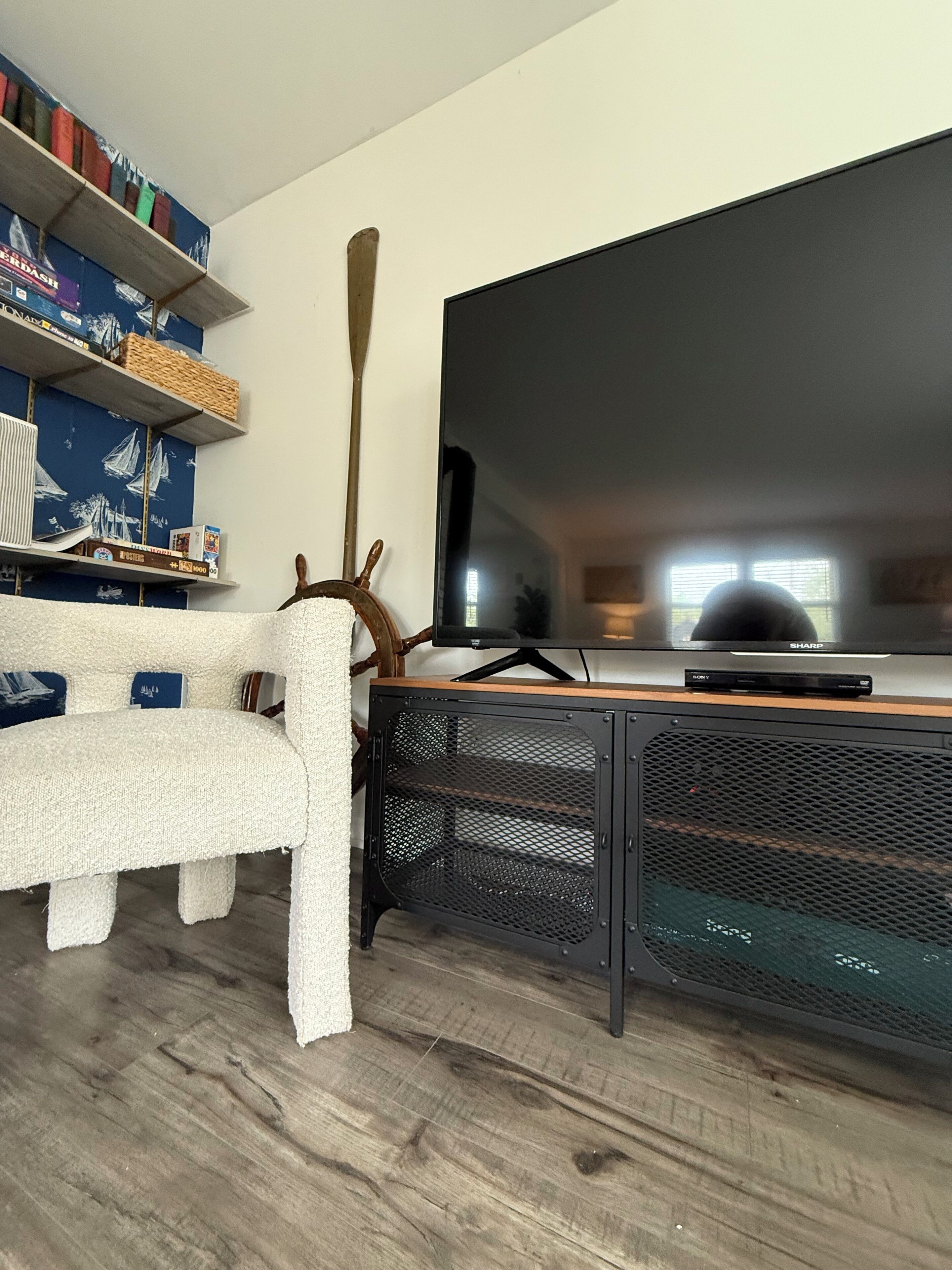 A modern living room with a white sofa, a wooden coffee table, a large flat-screen TV, and a bookshelf with various items.