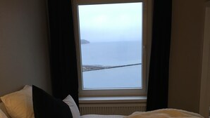 A hotel room with a large bed, a window with a view of the sea, and a radiator below the window.