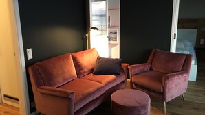 A modern living room with a dark wall, a wooden floor, a pink sofa, a matching armchair, and a small ottoman.