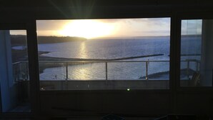 A room with a large window overlooking a body of water during sunset.