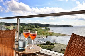 A table with two glasses of red wine and a metal container on a balcony overlooking a body of water and greenery. - Marina Apartment (Glücksburg (Ostsee))