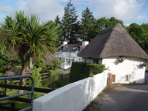 Ein Haus mit einem reetgedeckten Dach und weißer Fassade, umgeben von viel Grün und einem Holzzaun.