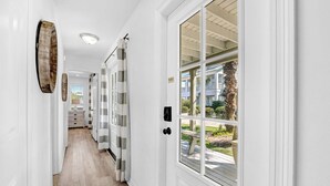 A hallway with a wooden floor, white walls, and a large window with a view of a building and palm trees. - Gulf view, Steps to beach, heated pool, walk to restaurants (Destin)