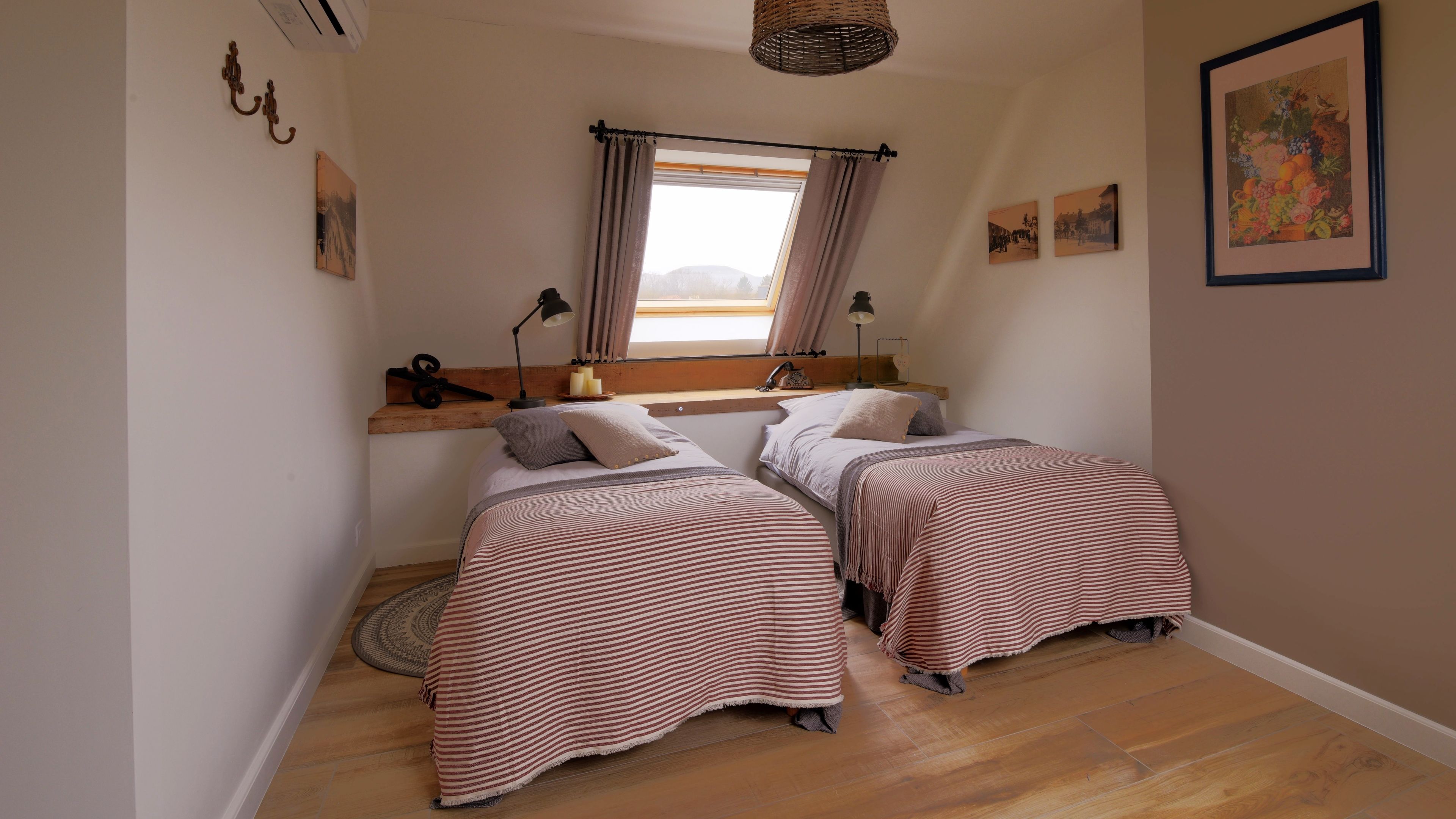A bedroom with two beds, a skylight, a wooden shelf, and a hanging light fixture.