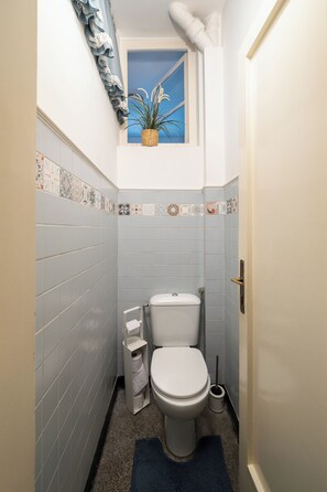 Un baño pequeño con inodoro, una ventana con una planta y un revestimiento de azulejos.