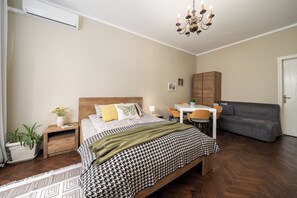 Un dormitorio con cama, mesita de noche, lámpara y un sofá gris.