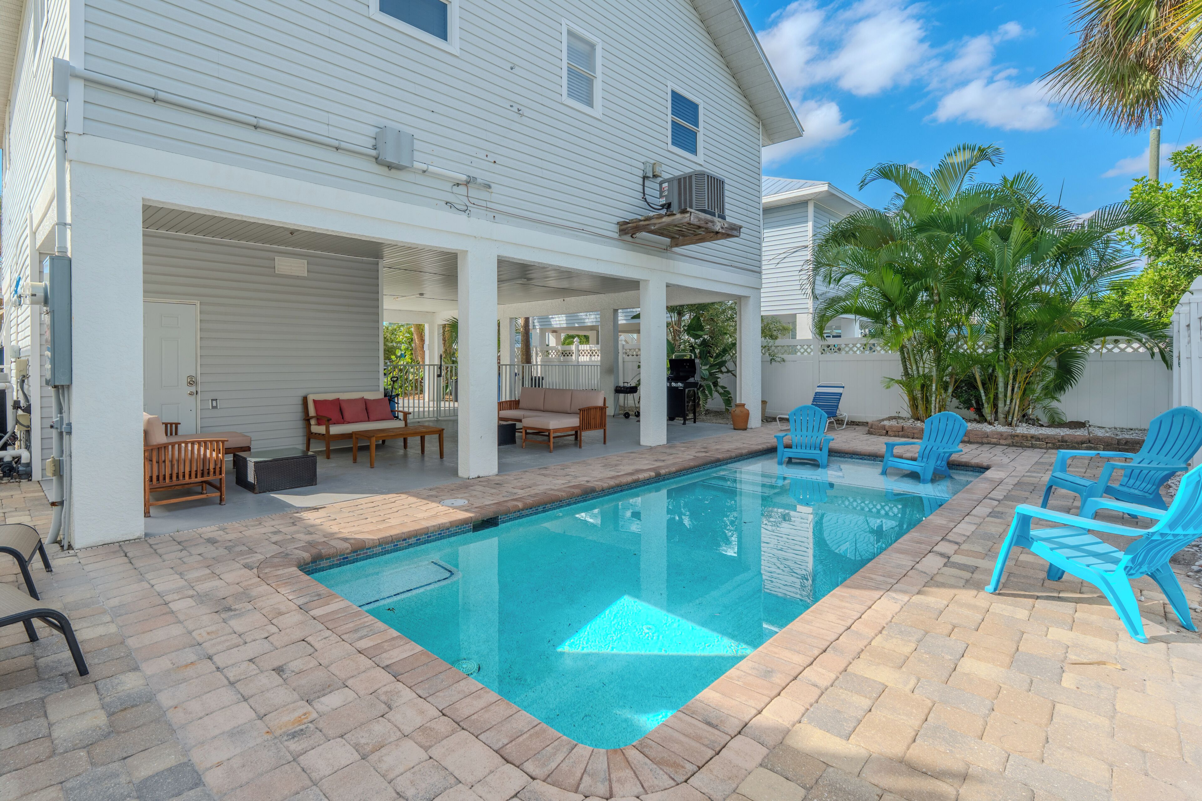 Une piscine résidentielle avec un patio couvert, du mobilier d’extérieur et une maison blanche.