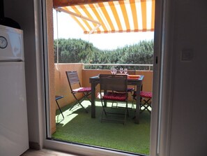 A balcony with a table and chairs, a clock, and a view of trees. - RESIDENCE IN SEASIDE (La londe les maures)