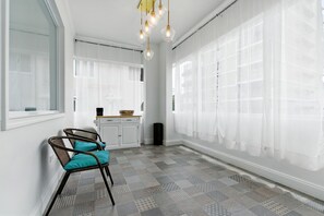 A spacious room with a patterned floor, white walls, and a large window with sheer curtains.