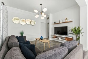 A modern living room with a grey sofa, a wooden coffee table, and a flat-screen TV on a white wall.