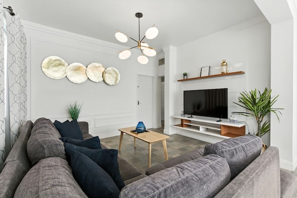 Un salon moderne avec un canapé gris, une table basse en bois et un téléviseur à écran plat fixé à un mur blanc.