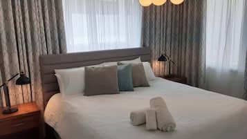 Ein Hotelzimmer mit einem großen Bett, zwei Nachttischen, einer Lampe und einem Satz Handtücher.