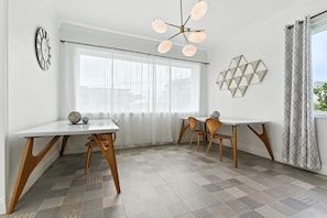 Une pièce moderne avec une table et des chaises blanches, une décoration murale aux motifs géométriques et un sol à motifs.