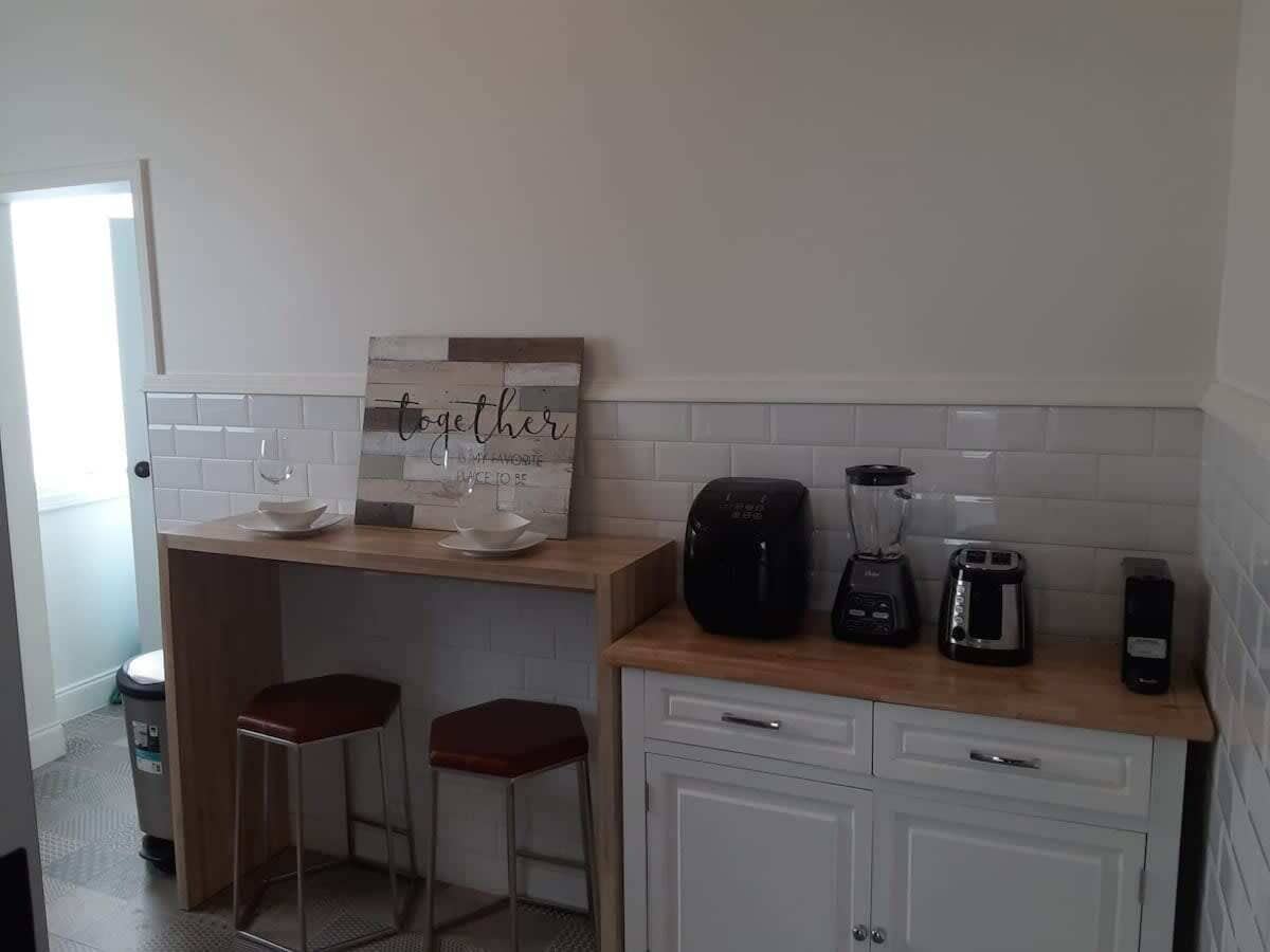 Una cocina con encimera de madera, una licuadora, un tostador y dos taburetes.