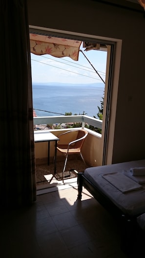 Una habitación con una cama, una silla y una mesa. Se ve el mar a través de una puerta abierta.