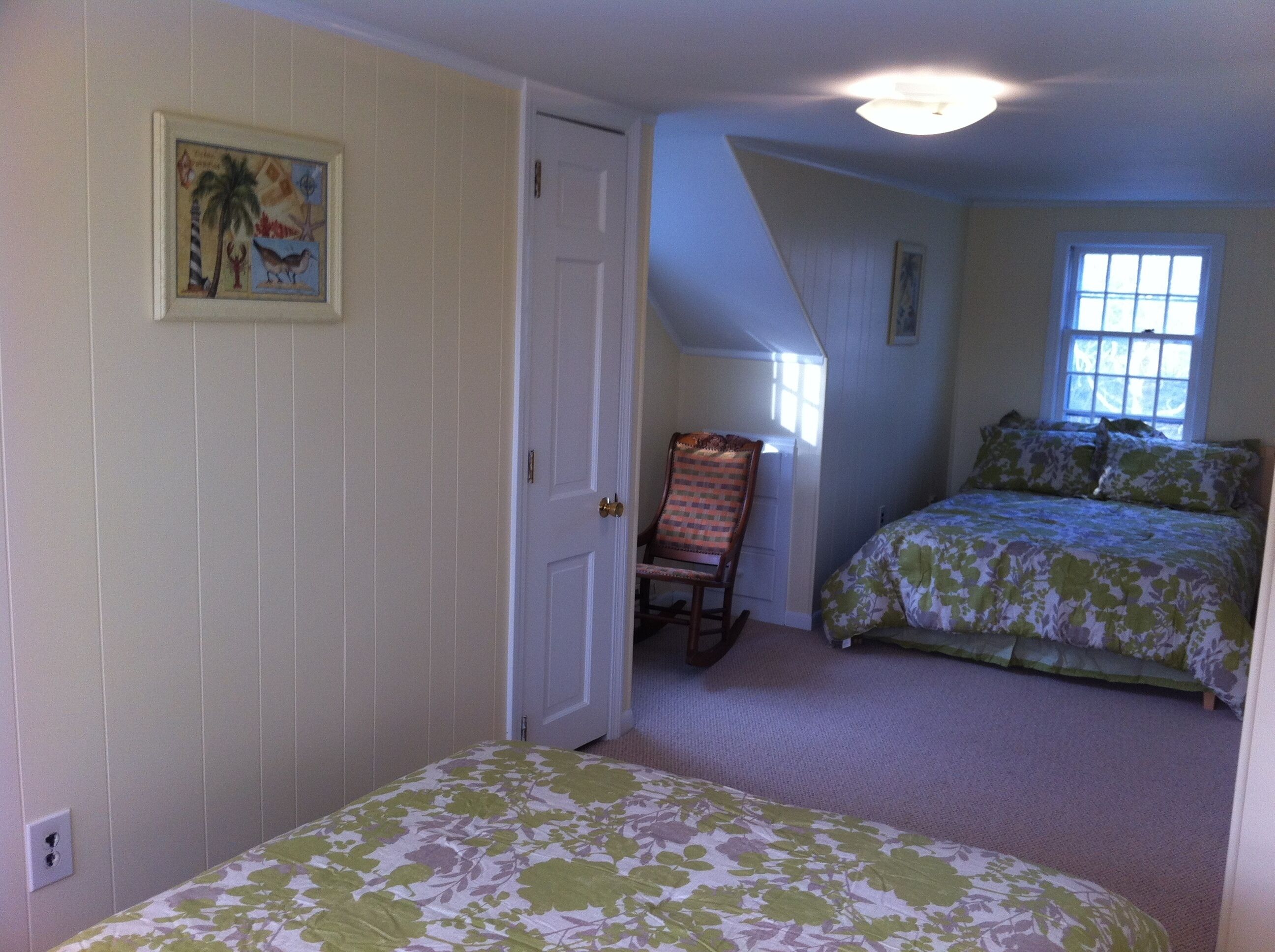 A bedroom with two beds, a chair, a door, and a window.
