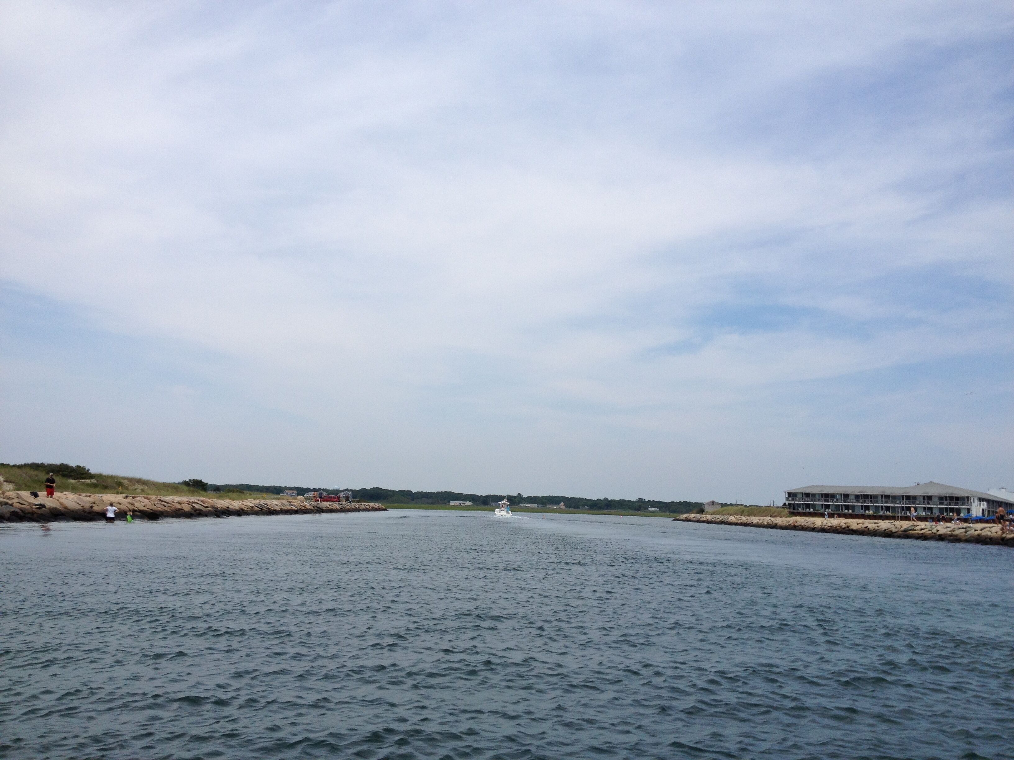A calm river with a boat in the distance, a rocky shoreline, and a building on the right.