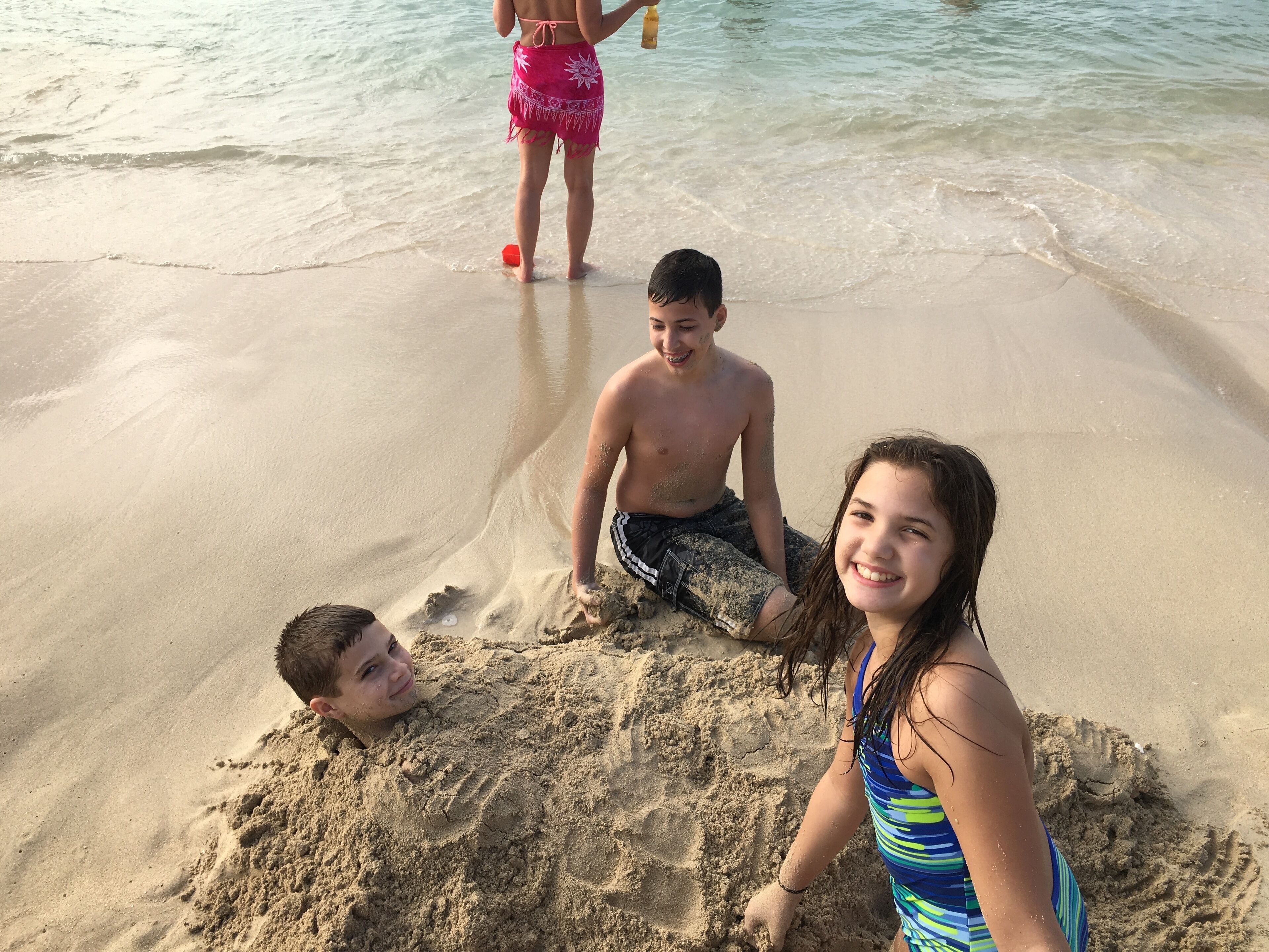 Three people on a sandy beach with clear water in the background.