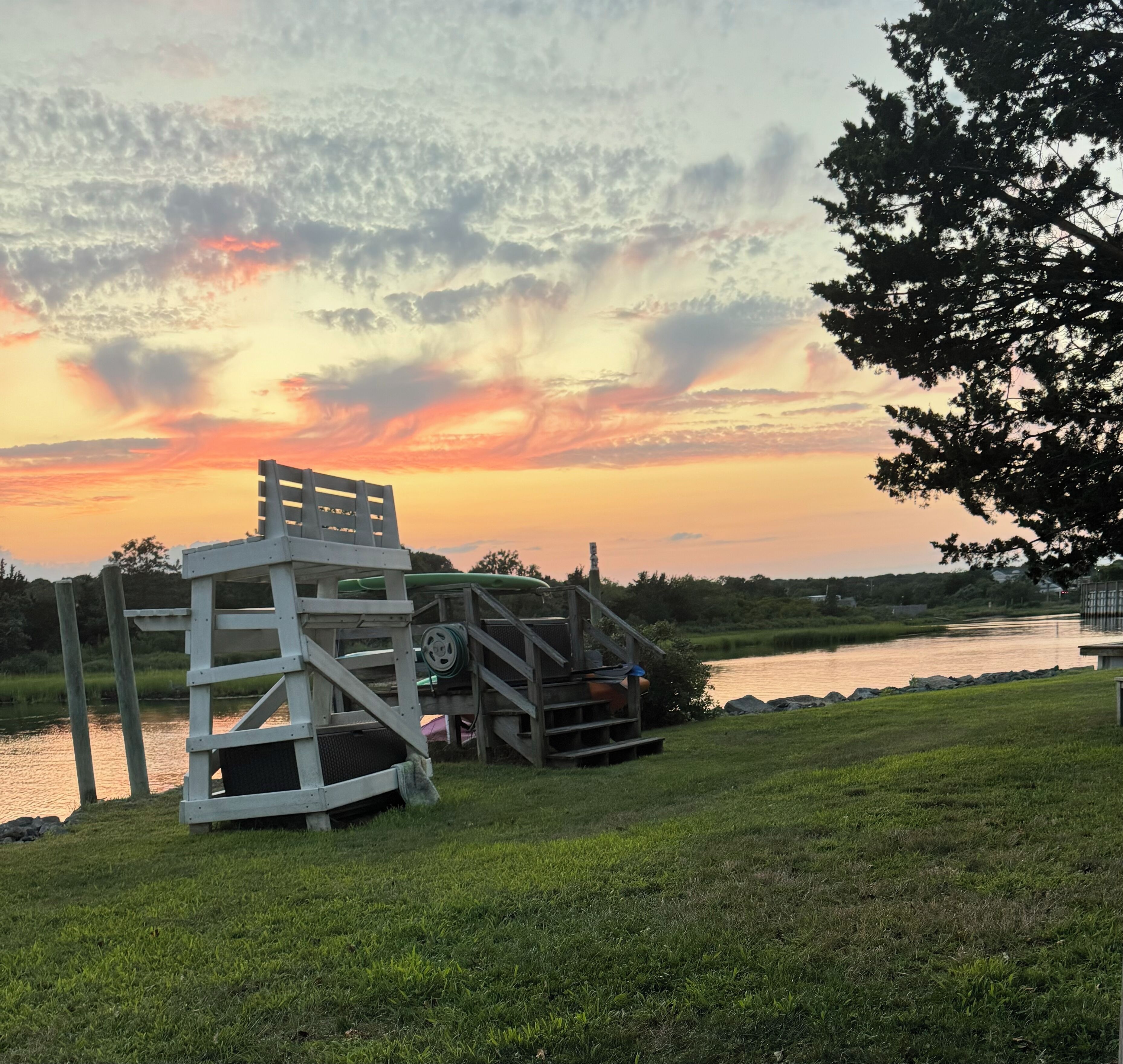 A wooden structure with steps leading to a platform, situated near a body of water with a sunset in the background.