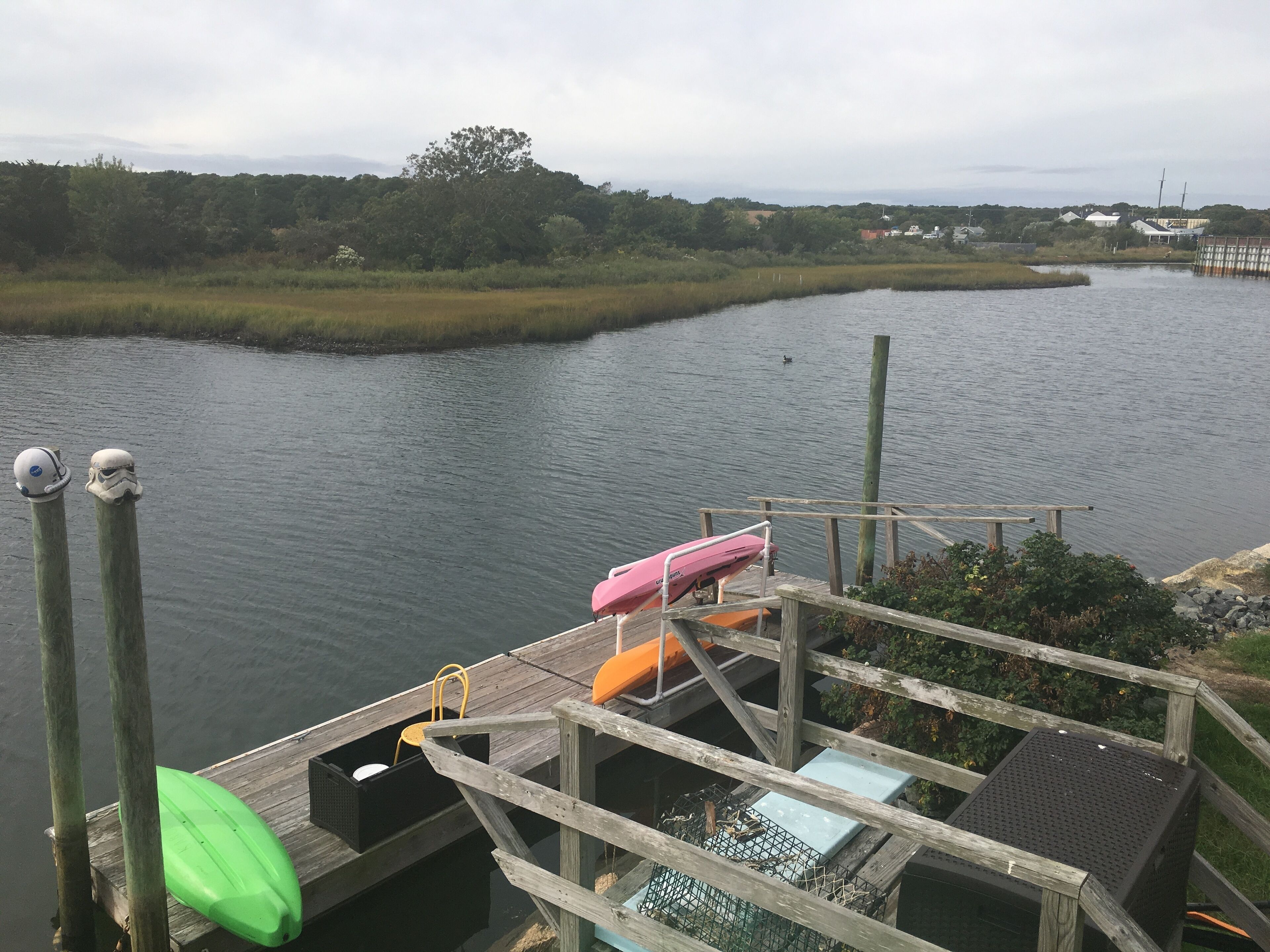 A wooden dock with a kayak and a paddleboard, a small boat, and a lifebuoy.