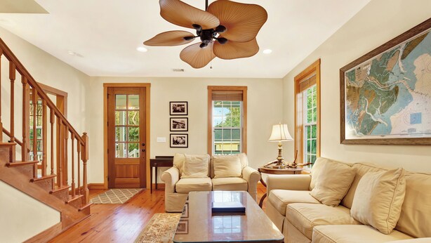 A spacious living room with a wooden staircase, a large ceiling fan, and a map on the wall.