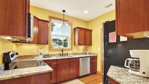 A kitchen with wooden cabinets, granite countertops, a stainless steel dishwasher, and a coffee maker.