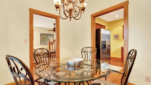 A dining area with a glass table surrounded by metal chairs, a chandelier, and wooden flooring.