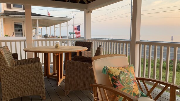 Un espacio al aire libre techado con mobiliario de mimbre, una mesa de madera y vista al frente marítimo.