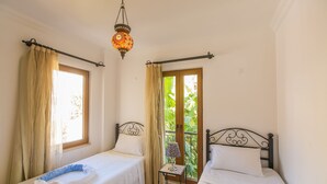 Ein Zimmer mit zwei Einzelbetten, einem kleinen Tisch mit einer Lampe und einem Balkon mit Blick auf Grünflächen.