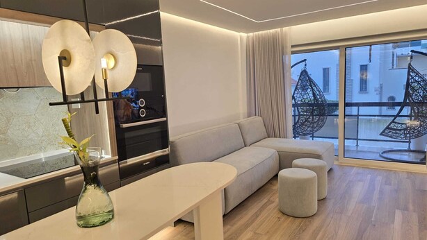 A modern living room with a sofa, ottomans, a dining table, and a kitchen area with a Bosch oven.