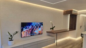 A modern living room with a flat-screen TV mounted on the wall, a wooden bench, and a potted plant.