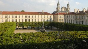 Un grand bâtiment historique à la façade symétrique, doté d’une cour intérieure avec une statue, et d’une église dont les deux tours se dressent à l’arrière-plan.