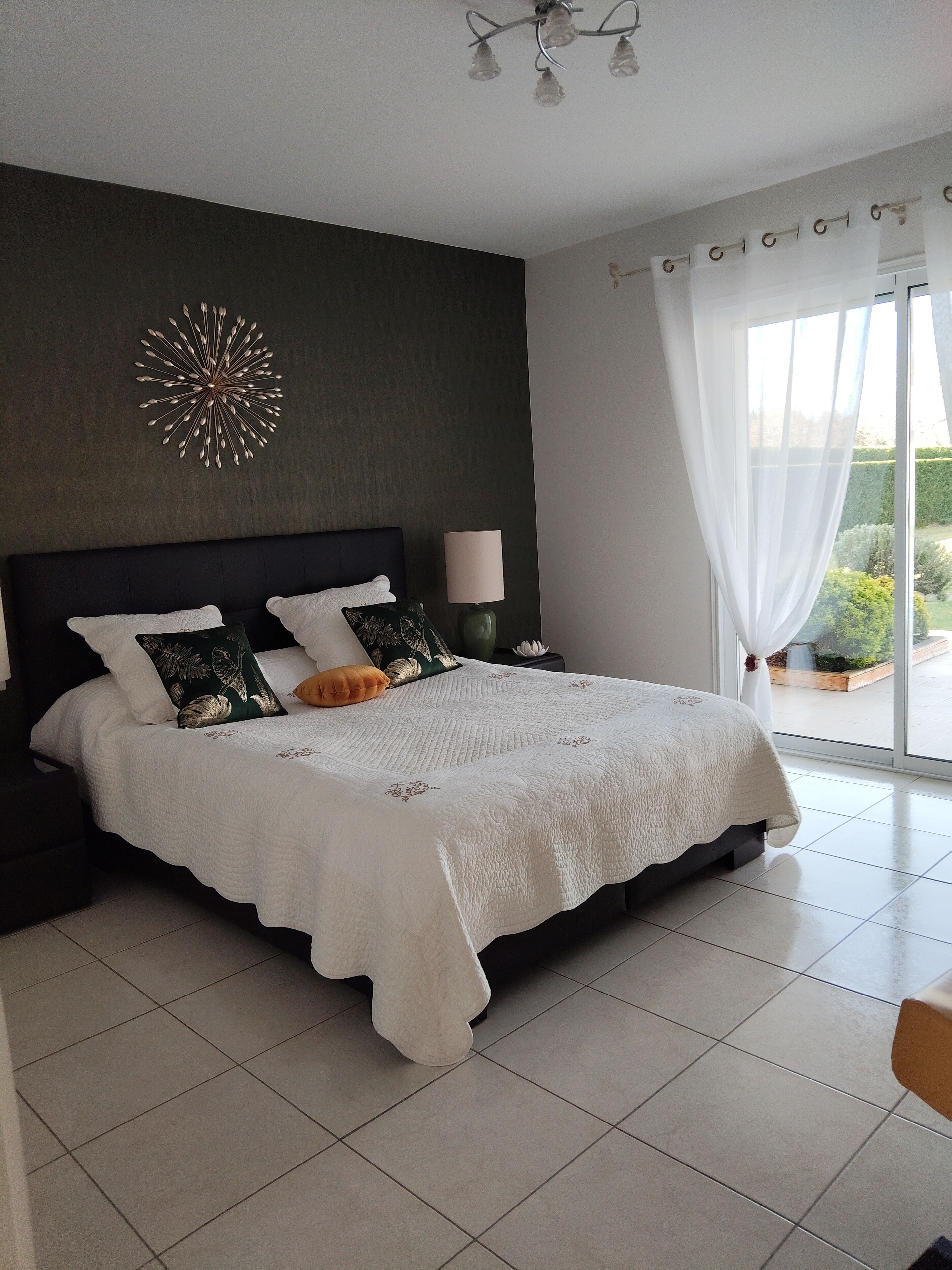 Een slaapkamer met een groot bed, nachtkastje, lamp en decoratief wandobject.