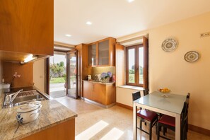Uma cozinha moderna com armários de madeira, bancada de mármore e um espaço de jantar com mesa de vidro e cadeiras vermelhas.