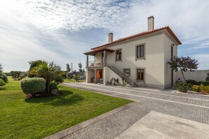 Uma casa de dois andares com telhado em telhas, varanda e entrada com calçada.