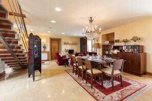 Uma sala de jantar com um lustre, mesa de madeira, cadeiras e um tapete vermelho.