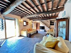 A rustic living room with exposed wooden beams, a sofa, a television, and a staircase leading to another level.