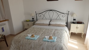 A neatly made bed with a patterned bedspread, two pillows, and two folded towels on the bed. There are two bedside tables with lamps and a small cabinet with a picture on the wall above the bed. - Roccascalegna, Chieti (Roccascalegna)