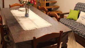 A dining area with a wooden table, chairs, a vase with flowers, a staircase, and a sofa with a checkered cover. - Roccascalegna, Chieti (Roccascalegna)