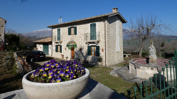 A stone house with a balcony, a flower bed with purple flowers, and a statue in the foreground. - Roccascalegna, Chieti (Roccascalegna)