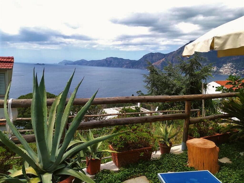 A balcony with potted plants, a wooden fence, and a view of the sea and mountains.