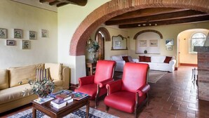 Amplia sala de estar con techo alto, vigas de madera a la vista y un arco de ladrillo. Hay dos sofás y una mesa de centro con libros y un florero.
