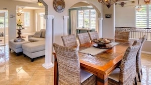 A dining area with a wooden table and wicker chairs, a sofa, and a decorative wall piece. - Mountaintop Villa with Spectacular Sunset View of Caribbean  (rincon)