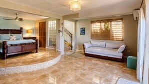 A bedroom with a bed, a sitting area with a sofa, a staircase, and a ceiling fan. - Mountaintop Villa with Spectacular Sunset View of Caribbean  (rincon)