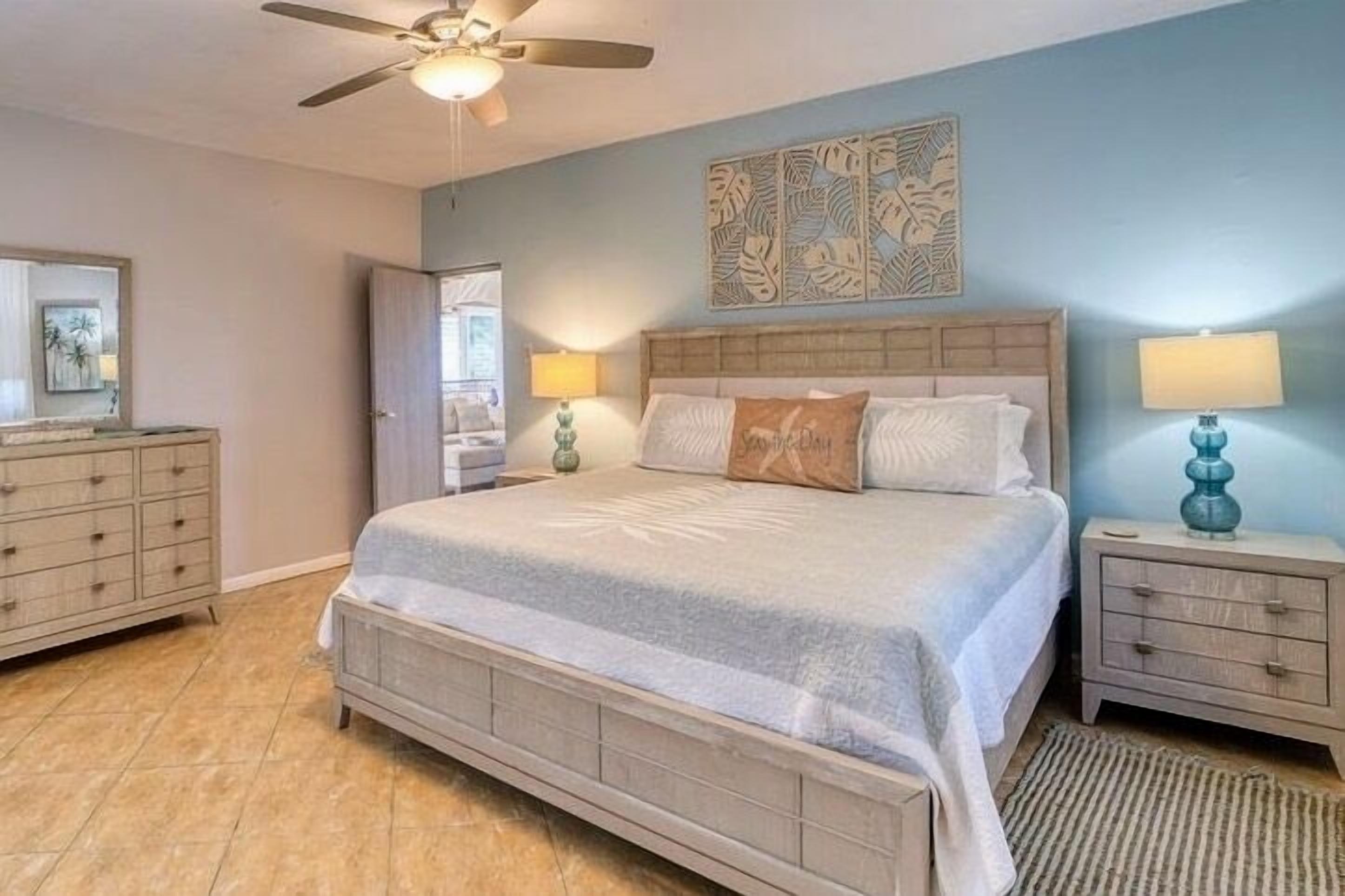 A bedroom with a large bed, two bedside tables, a ceiling fan, and a wall art piece.