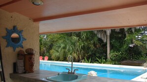 A poolside area with a concrete counter, a blue sink, and a decorative mirror.