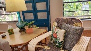 A room with a wicker chair, a table, a blue cabinet, and a window with a view of greenery.