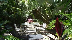 An outdoor patio with a round table and chairs, surrounded by lush tropical plants.